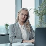 Professional businesswoman at a desk in a bright office with a laptop and notebook.